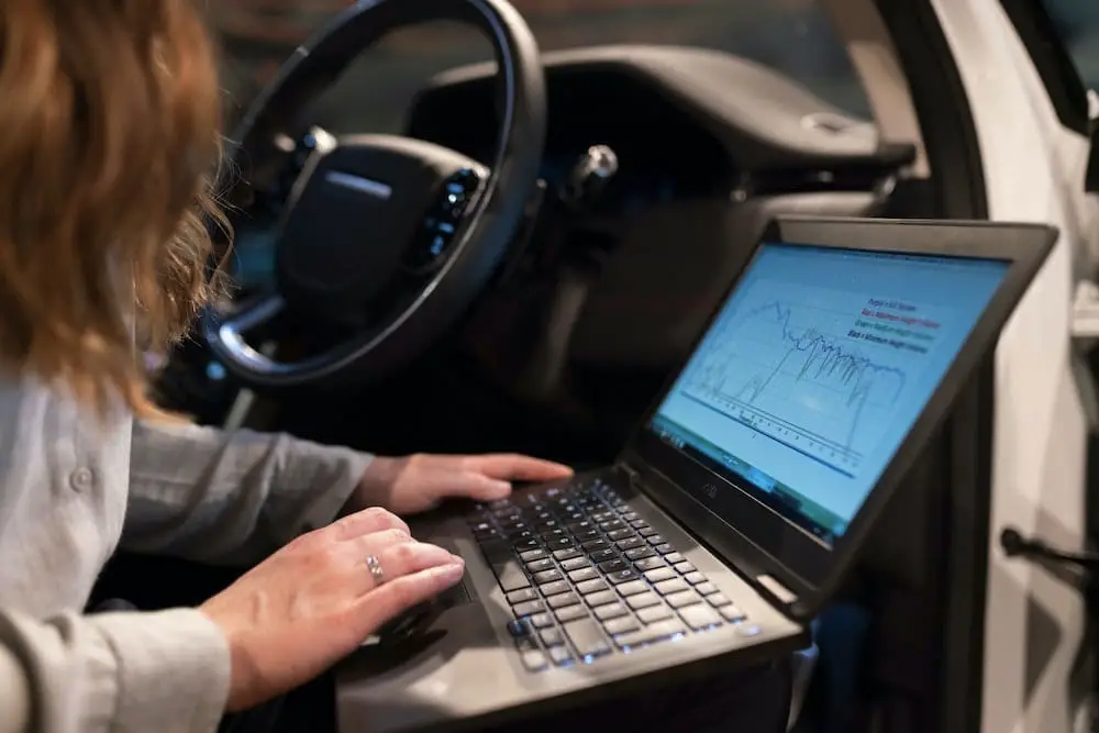 Lady on laptop checking fleet management data on a car